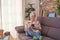 Smiling senior woman sitting on sofa at home using phone. White-haired elderly enjoying technology and retirement. Bright light