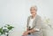 Smiling senior woman sitting on sofa and looking at camera. Awaken old woman with grey hair and pajamas in the early morning light