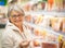 A smiling senior woman at the supermarket chooses which ham to buy. Many products on offer in the refrigerated counter