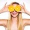 Smiling sensual woman holding slices of oranges to her eyes.