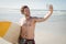 Smiling shirtless man taking selfie with surfboard at beach