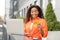 Smiling shocked emotional millennial black woman looking at credit card with computer in city