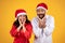 Smiling shocked mature latin man and lady in Santa hats, celebrating holiday together