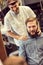 Smiling skillful barber making haircut too bearded customer