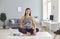 Smiling slender asian girl sitting on the table next to a laptop with a yoga mat in her hands.