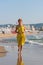 Smiling slender lady in a yellow sundress runs along the sand of the sea beach.