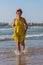 Smiling slender lady in a yellow sundress runs along the water of the sea beach.