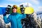 Smiling snowboarder posing carrying snowboard on shoulders at ski resort near forest before backcountry freeride and