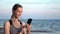 Smiling sports woman listening music earphones smartphone audio application running sunset sea beach