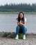 Smiling sports Yakut Asian young girl sitting on the stone Bank of the river Viluy in the Northern taiga firs with his han