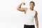 Smiling sportsman flex biceps, showing strong arm mucles and looking satisfied, workout in gym, white background