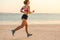 smiling sportswoman in earphones with smartphone in running armband case jogging on beach with sea
