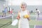 Smiling sporty elderly woman standing in indoor pickleball court