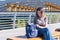 A smiling student girl with glasses, opening her backpack, looking for something in her bag, sitting outdoors on a bench