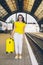 smiling stunning woman with yellow suitcase on wheels at railway station