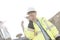 Smiling supervisor using walkie-talkie at construction site against clear sky