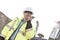 Smiling supervisor using walkie-talkie at construction site against clear sky