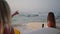 Smiling surfer girls holding surfboards standing on beach at sunrise pointing at waves. Cheerful female surfers by ocean