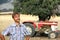 Smiling tanned farmer stands near the old tractor in the middle of a plowed field. Countryside in Cyprus