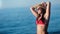 Smiling tanned woman in bikini wearing hat having fun at sunset seascape medium shot