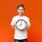 Smiling teen boy holding big clock, orange background