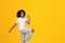 Smiling teen curly girl in white t-shirt dancing, has fun alone, isolated on yellow studio background