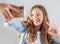 Smiling teen making selfie photo on smartphone over white background  cute girl