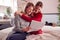 Smiling Teenage Daughter Wearing Pyjamas Looking At School Exam Report With Mother In Bedroom