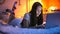 Smiling teenage girl lying on bed at night and chatting on laptop