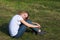 Smiling teenage girl in a white t-shirt sits on the grass with her head on her knees