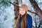 Smiling teenager girl in a blue down jacket and beige hat on a background of snowy fir branches. Winter, Christmas, New Year