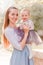 Smiling thirty-year-old woman holds beautiful baby girl in dress on a blurr background in a counter-light summer