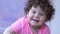 Smiling toddler with curly hair spends time in room on unfocused background