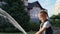 Smiling toothless girl in wheelbarrow with garden hose watering the backyard, summer outdoors