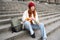 Smiling tourist, girl sits on stairs, rests on staircase, takes thermos from backpack, drinks hot coffee from flask