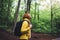 Smiling tourist traveler with backpack into road at summer green forest, view back girl hiker in yellow hoody looking and enjoying