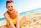 Smiling trendy woman in colorful dress sitting on beach