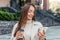 smiling uses a mobile phone and sits against the backdrop of an office building