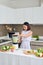 Smiling vegan Asian woman making a smoothie with fruit and vegetable in the kitchen