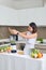 Smiling vegan Asian woman making a smoothie with fruit and vegetable in the kitchen