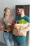 smiling vegan couple with paper bag full of fresh vegetables in kitchen