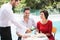 Smiling waiter serving red wine to couple