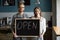 Smiling waiter and waitress holding chalkboard with open sign, p