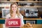 Smiling waitress showing signboard with open sign at cafe