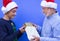 A smiling white-haired, white-bearded grandfather offers a Christmas present to his teenage grandson who is wearing a Christmas