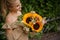 Smiling woman accurate holds bouquet with sunflowers in her hands.