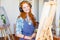 Smiling woman artist painting on canvas and listening to music