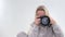 Smiling woman with camera close up against grey background Woman in a light tracksuit with a camera Takes pictures on
