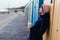 Smiling woman with closed eyes in warm clothes with a reusable cup with a hot drink near colorful beach booths and enjoying the