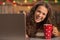 Smiling woman with cup of chocolate looking out from laptop